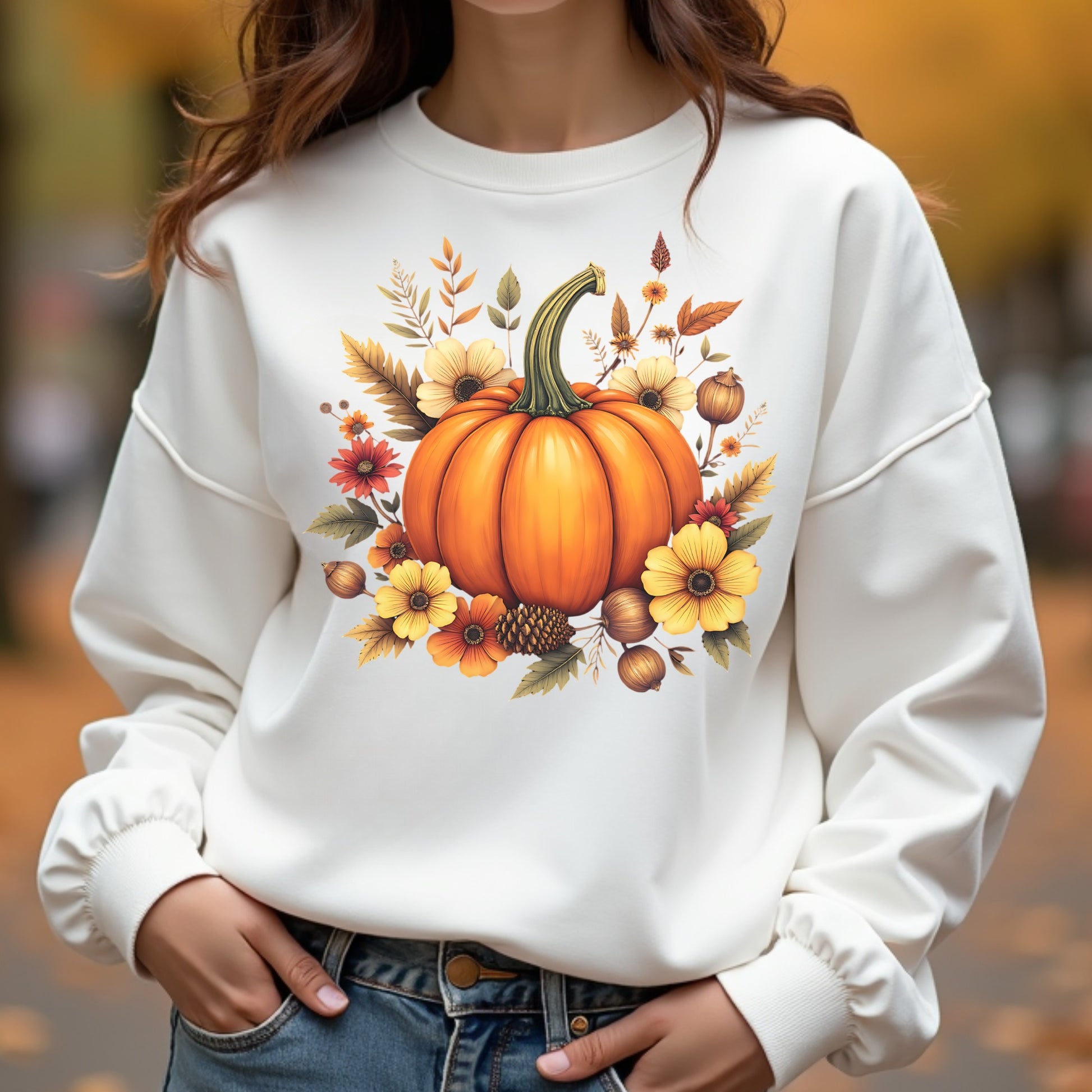 White sweatshirt with a pumpkin and autumn leaves design worn by a woman outdoors.