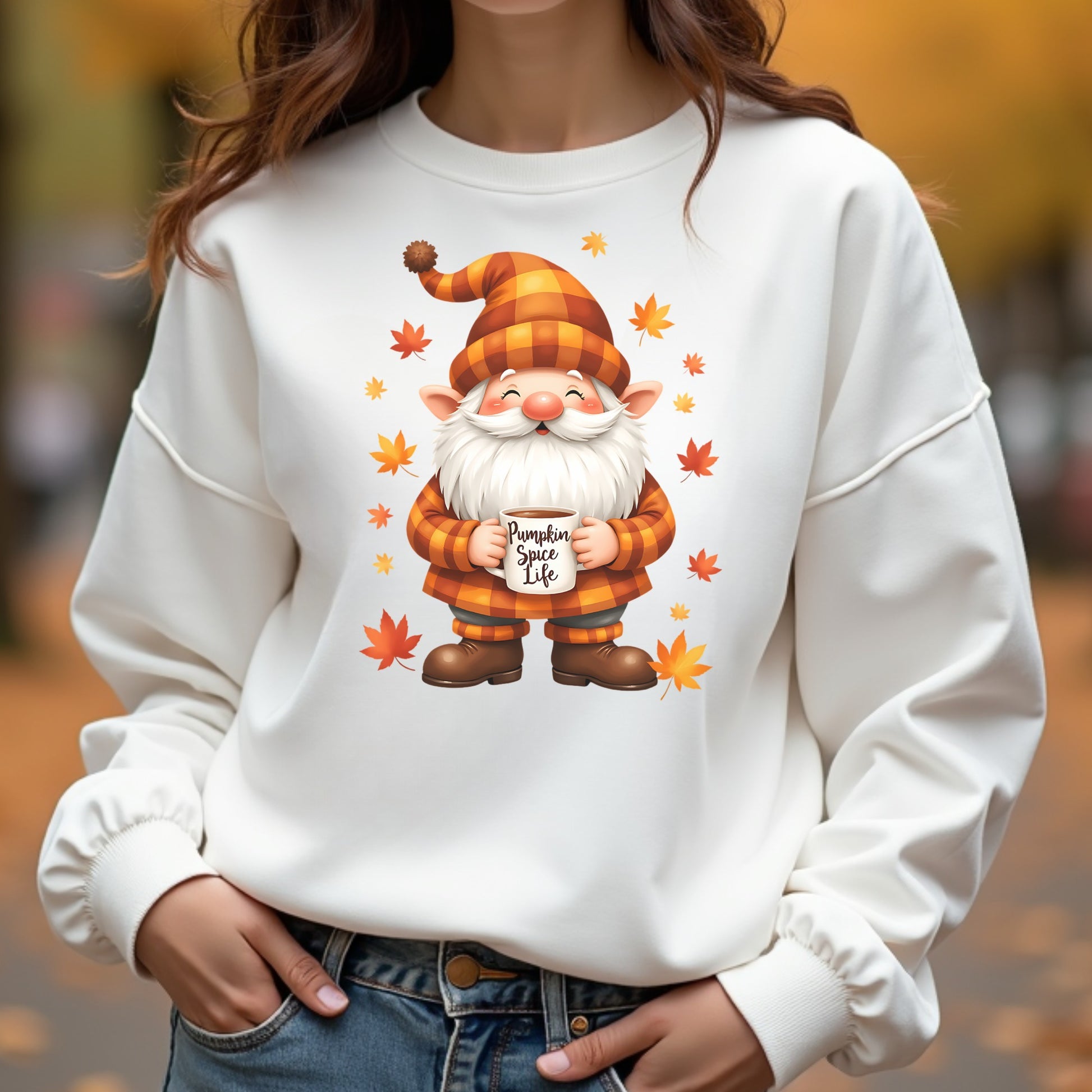 Woman wearing a white sweatshirt with a gnome graphic and 'Pumpkin Spice Life' text, standing outdoors with blurred autumn background.