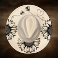 Round white hat with black floral and bee designs on a brown background