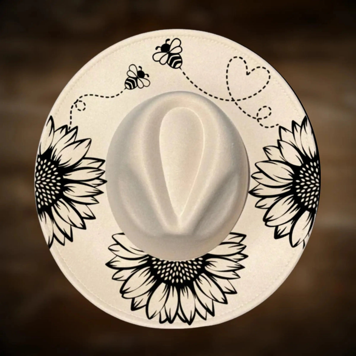 Round white hat with black floral and bee designs on a brown background