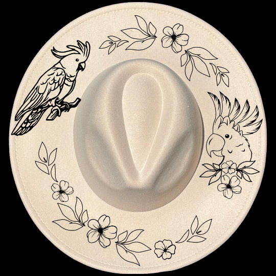 A beige wide brim hat with a burning design that includes a cockatoo and floral patterns around the edge.