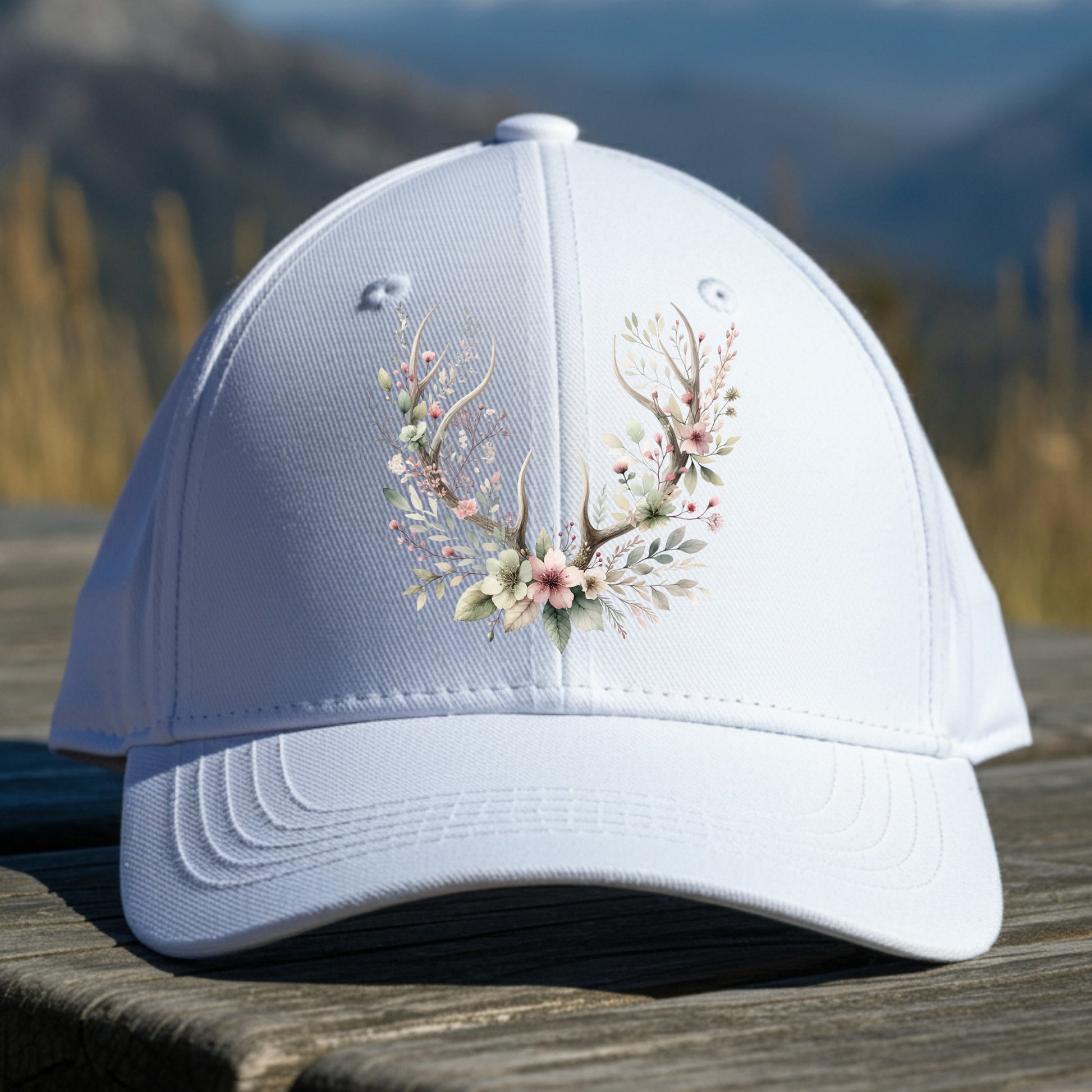 White cap with floral and antler design on a wooden surface with a mountain background
