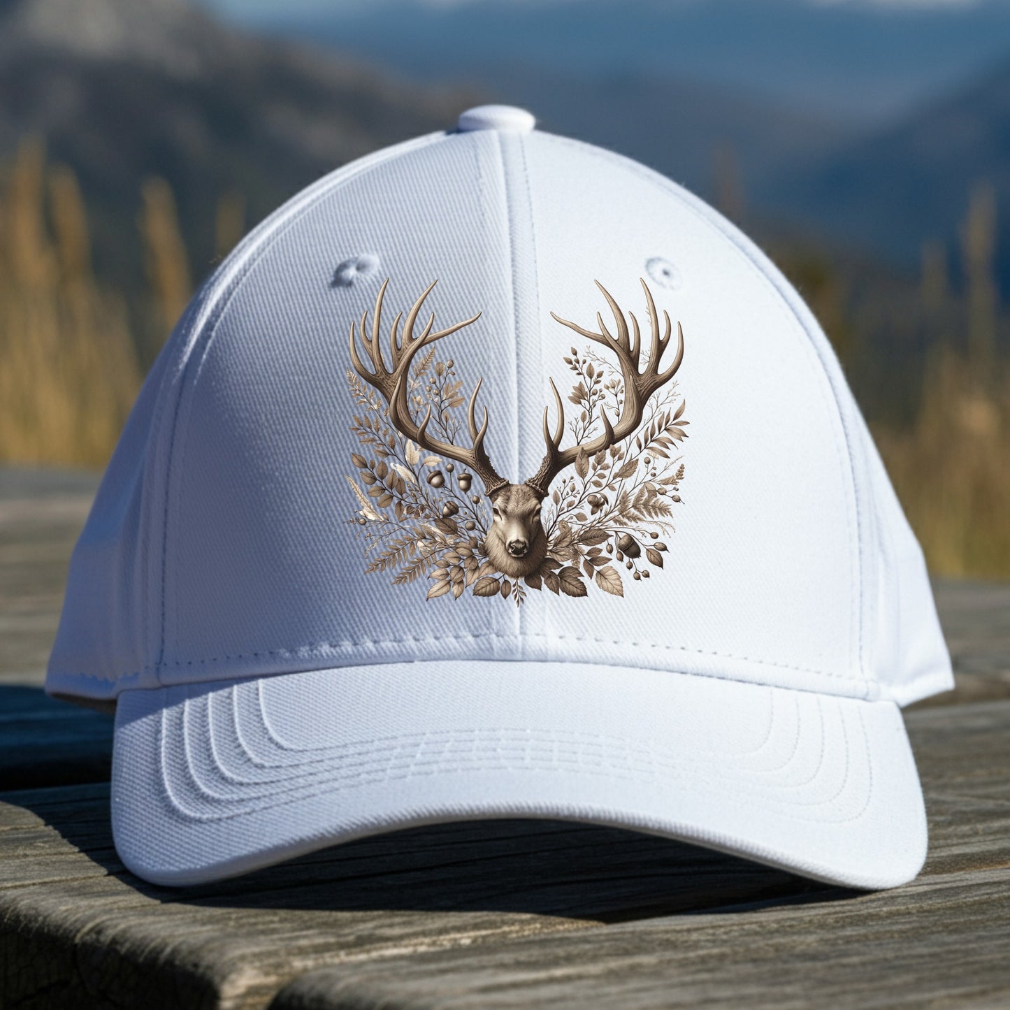 White cap with deer head and antlers design on a wooden surface with a mountain background