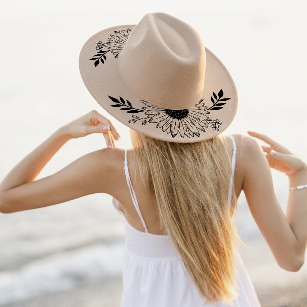 Woman wearing a wide brim hat with black floral designs on a beach.