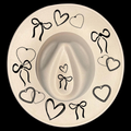A wide brim cowboy hat with black decorative bows and hearts on a black background