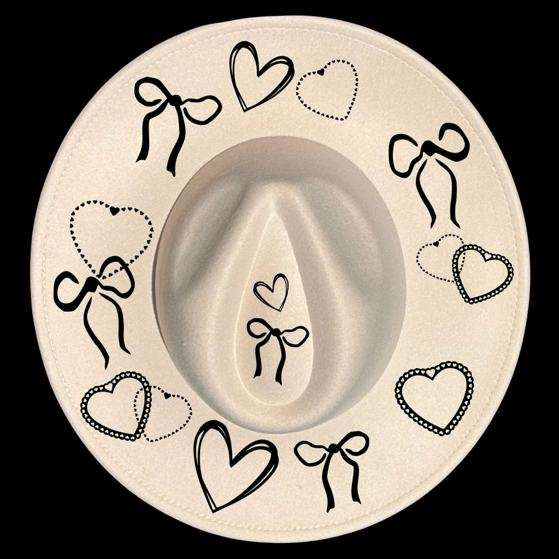A wide brim cowboy hat with black decorative bows and hearts on a black background
