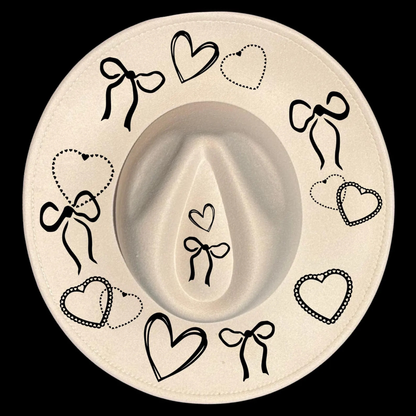 A wide brim cowboy hat with black decorative bows and hearts on a black background