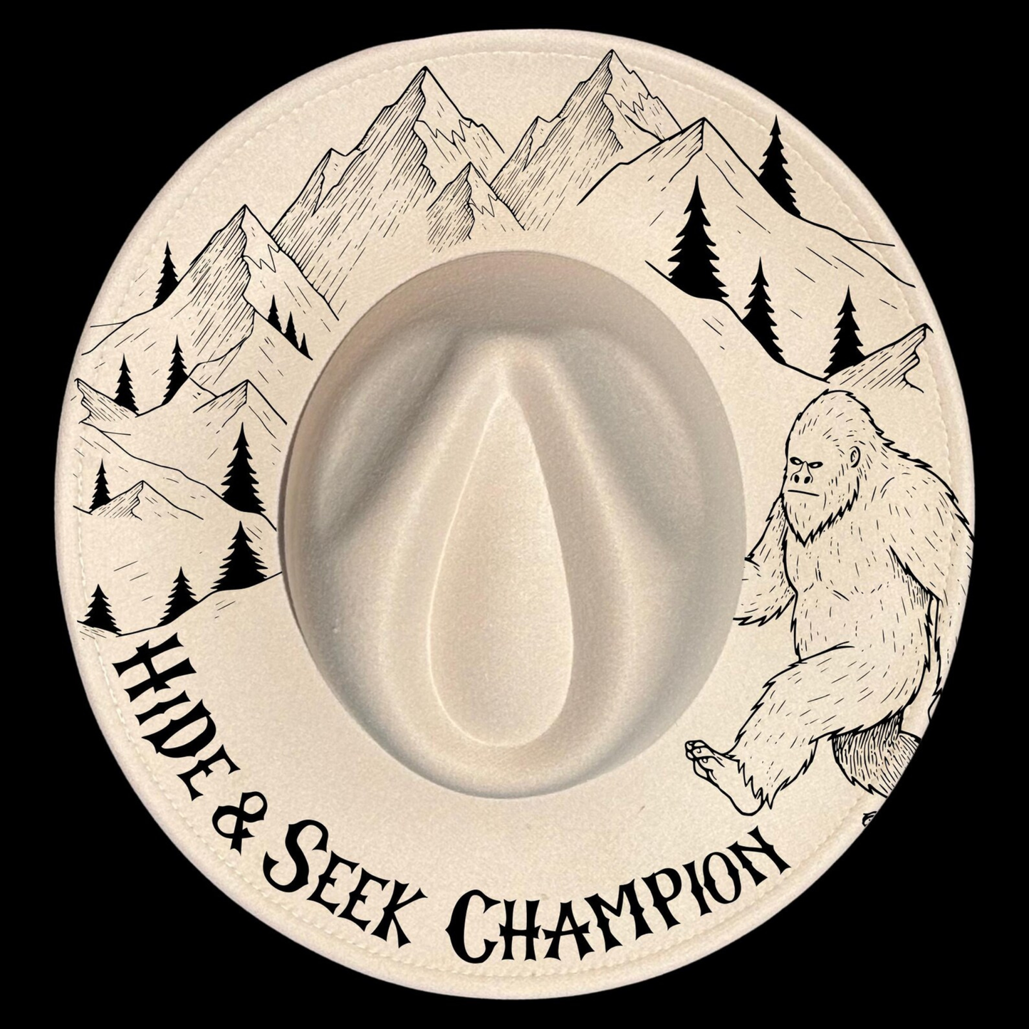 Wide brim hat with mountain, tree, and Bigfoot design, featuring 'Hide & Seek Champion' text.