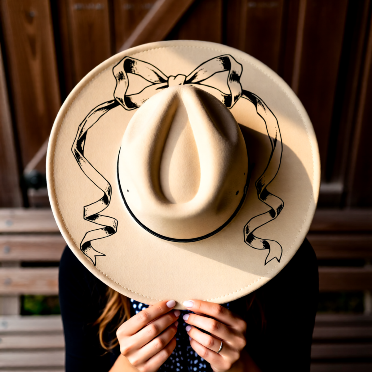 Beige cowboy hat with black ribbon design held by a person against a wooden background