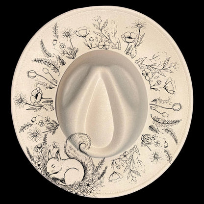 Wide brim hat with a floral design surrounded by line art of nature elements and a squirrel on a black background.