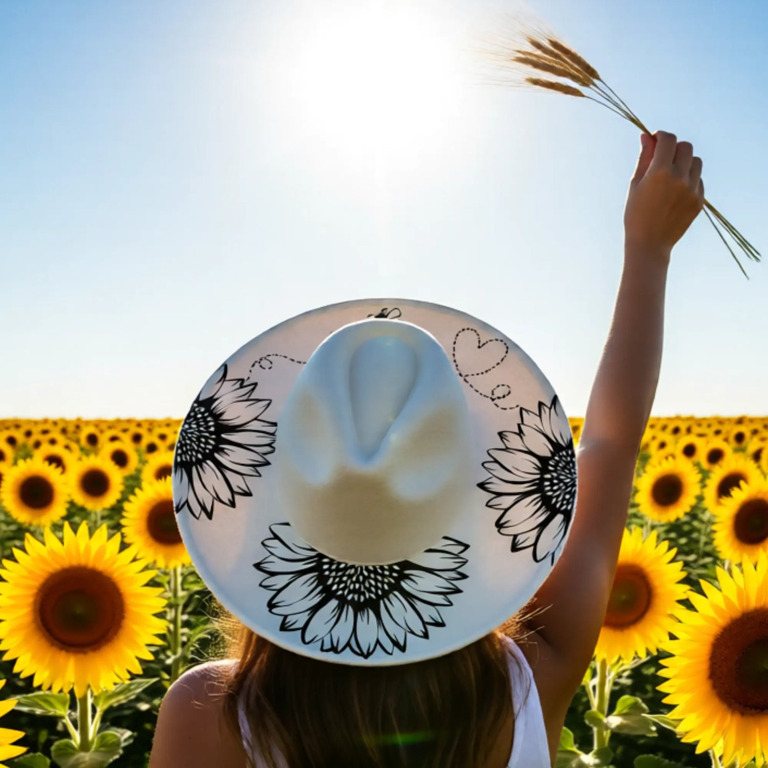 Person wearing a sun hat with sunflower design in a field of sunflowers.