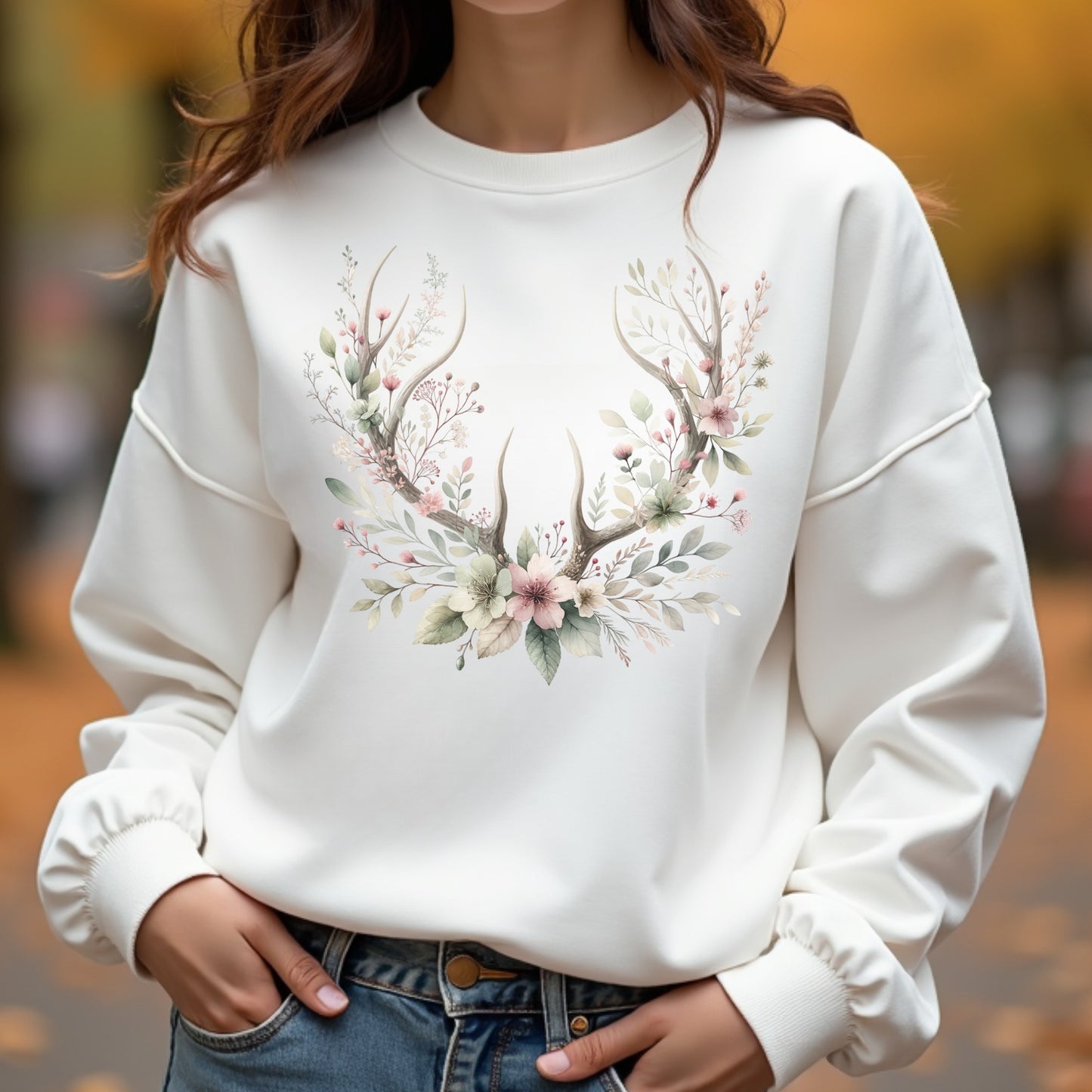 White sweatshirt with floral antler design worn by a woman outdoors.